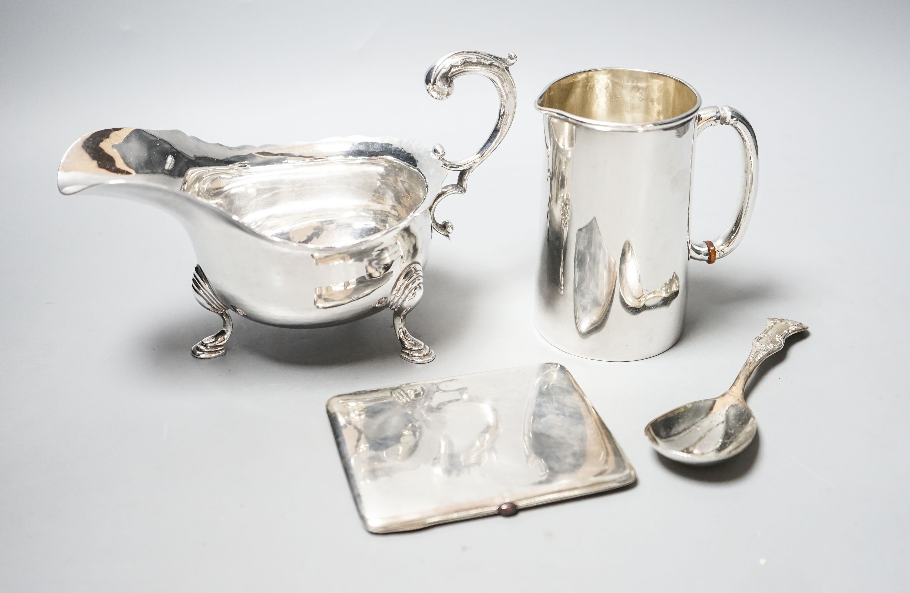 A George V silver sauceboat, a silver jug with military related inscription, a silver cigarette case and silver spoon